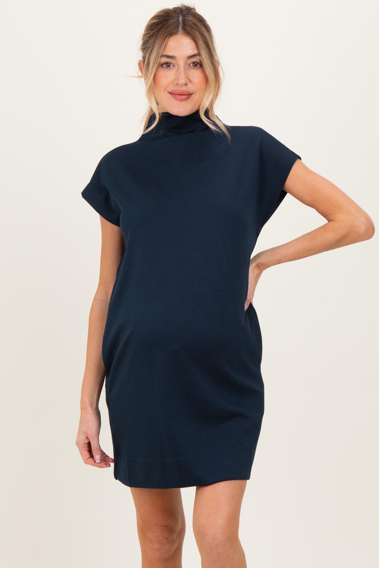 woman wearing a navy blue short sleeve maternity dress with a high neckline and relaxed fit, showing her baby bump