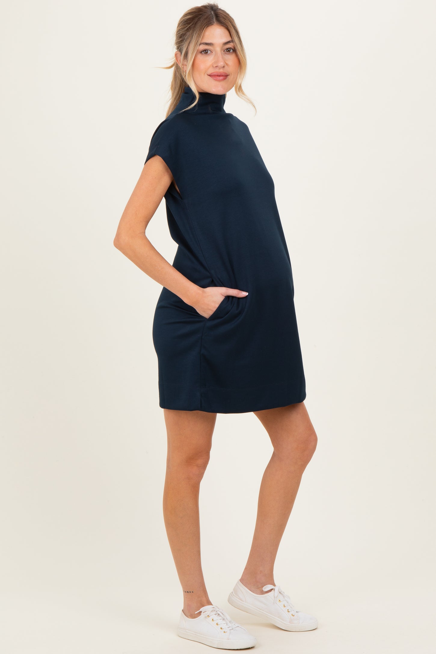 woman wearing a navy blue maternity dress with a high neck and side pockets, showing her baby bump