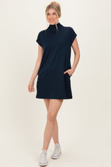 woman wearing a navy blue short sleeve mock neck dress with side pockets and white sneakers