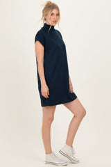 woman wearing a navy blue short sleeve dress with a high neckline and styled with white sneakers