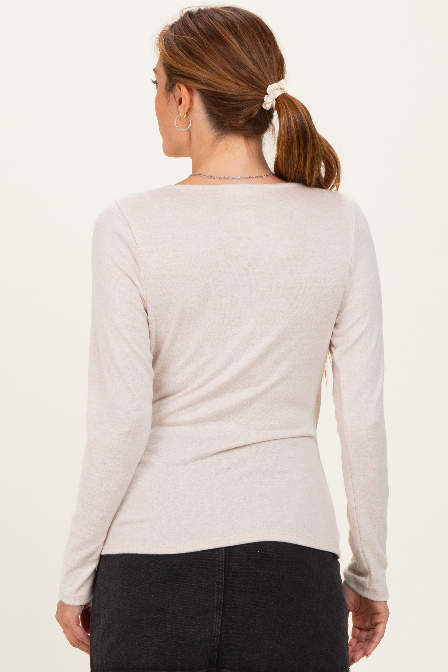 woman wearing a light beige long sleeve top with a fitted design and scoop neckline, viewed from the back