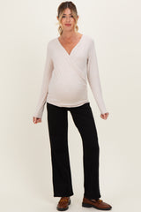 woman wearing a light pink long sleeve wrap maternity top and black flared pants with a visible baby bump