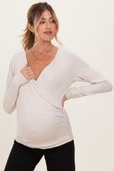 woman wearing a light pink long sleeve maternity top with a wrap design and holding her baby bump