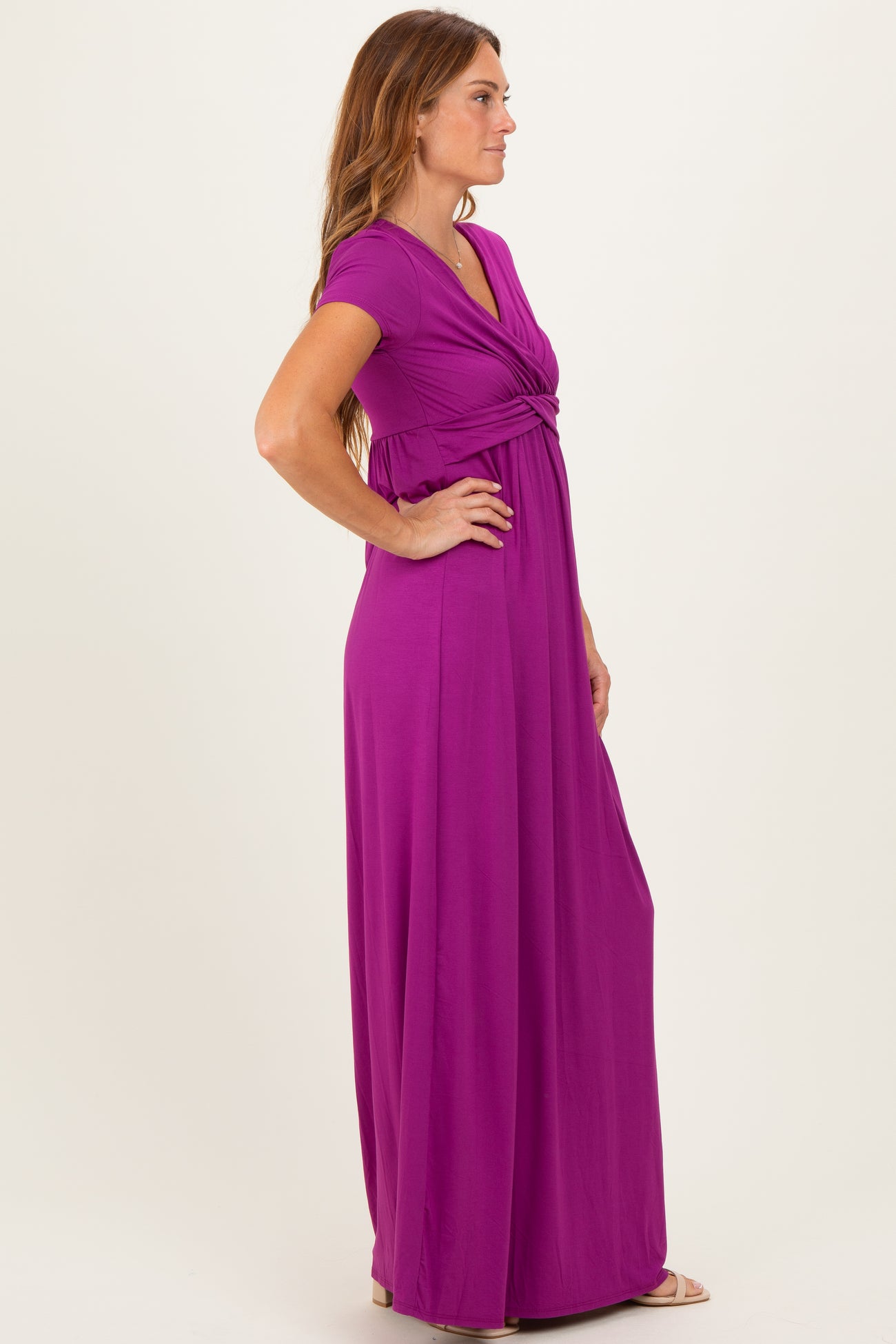 woman wearing a purple short sleeve maxi dress with a twisted front detail, standing in profile against a neutral background