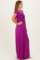 woman wearing a purple short sleeve maxi dress with a twisted front detail, standing in profile against a neutral background