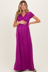 woman wearing a fuchsia short sleeve maternity maxi dress and holding her baby bump