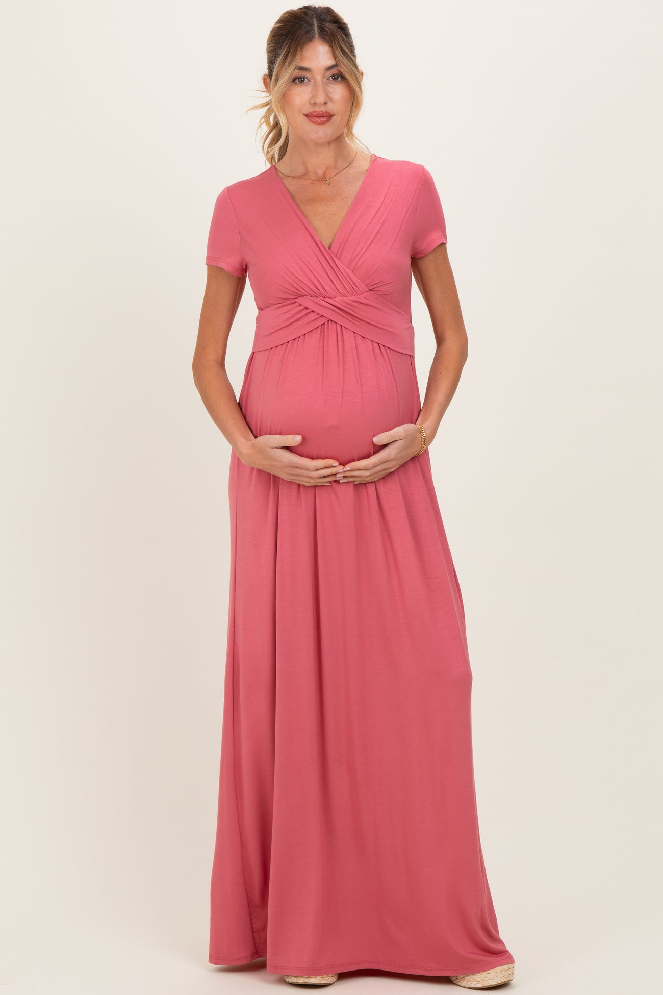 woman wearing a pink short sleeve maternity maxi dress and holding her baby bump