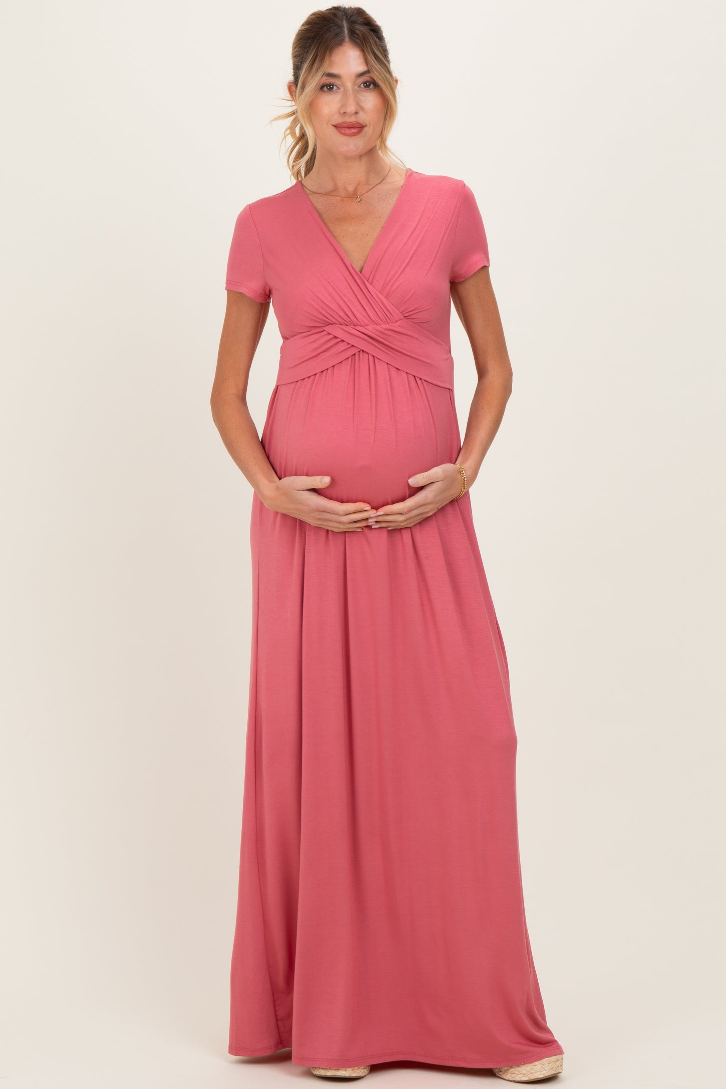 woman wearing a pink short sleeve maternity maxi dress and holding her baby bump