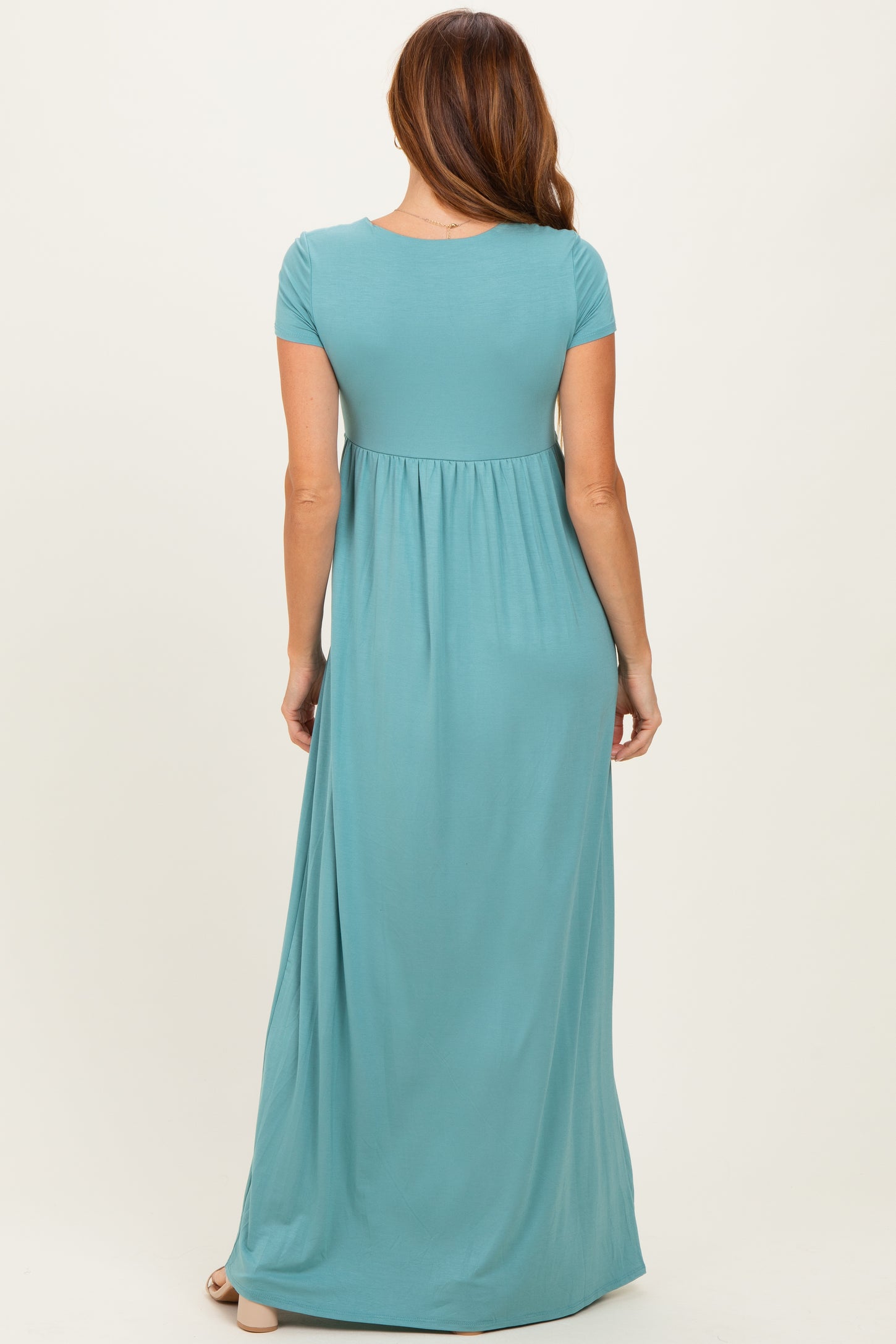 woman wearing a teal short sleeve maxi dress with a fitted bodice and flowing skirt seen from the back