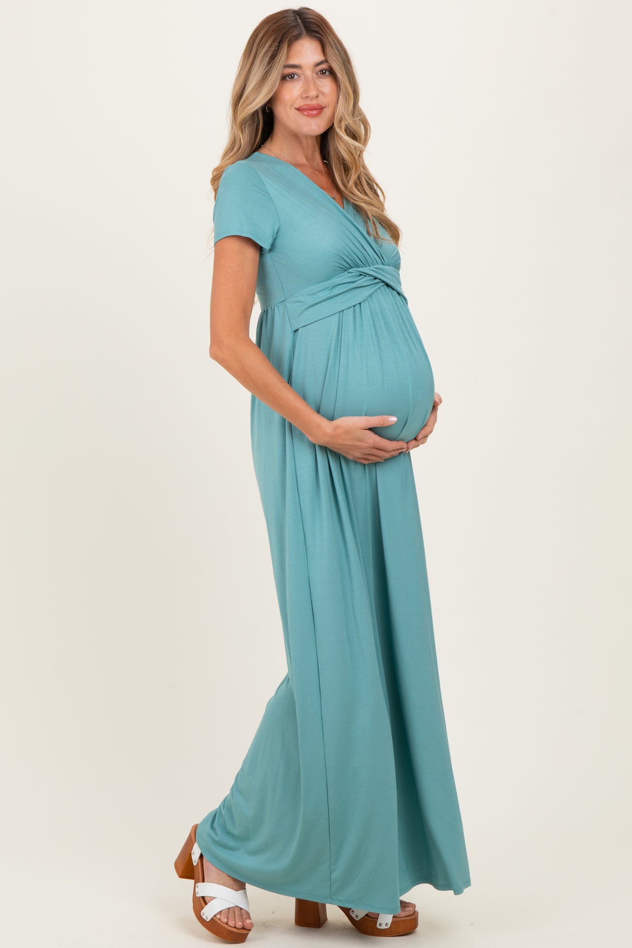woman wearing a teal short sleeve maternity maxi dress and holding her baby bump
