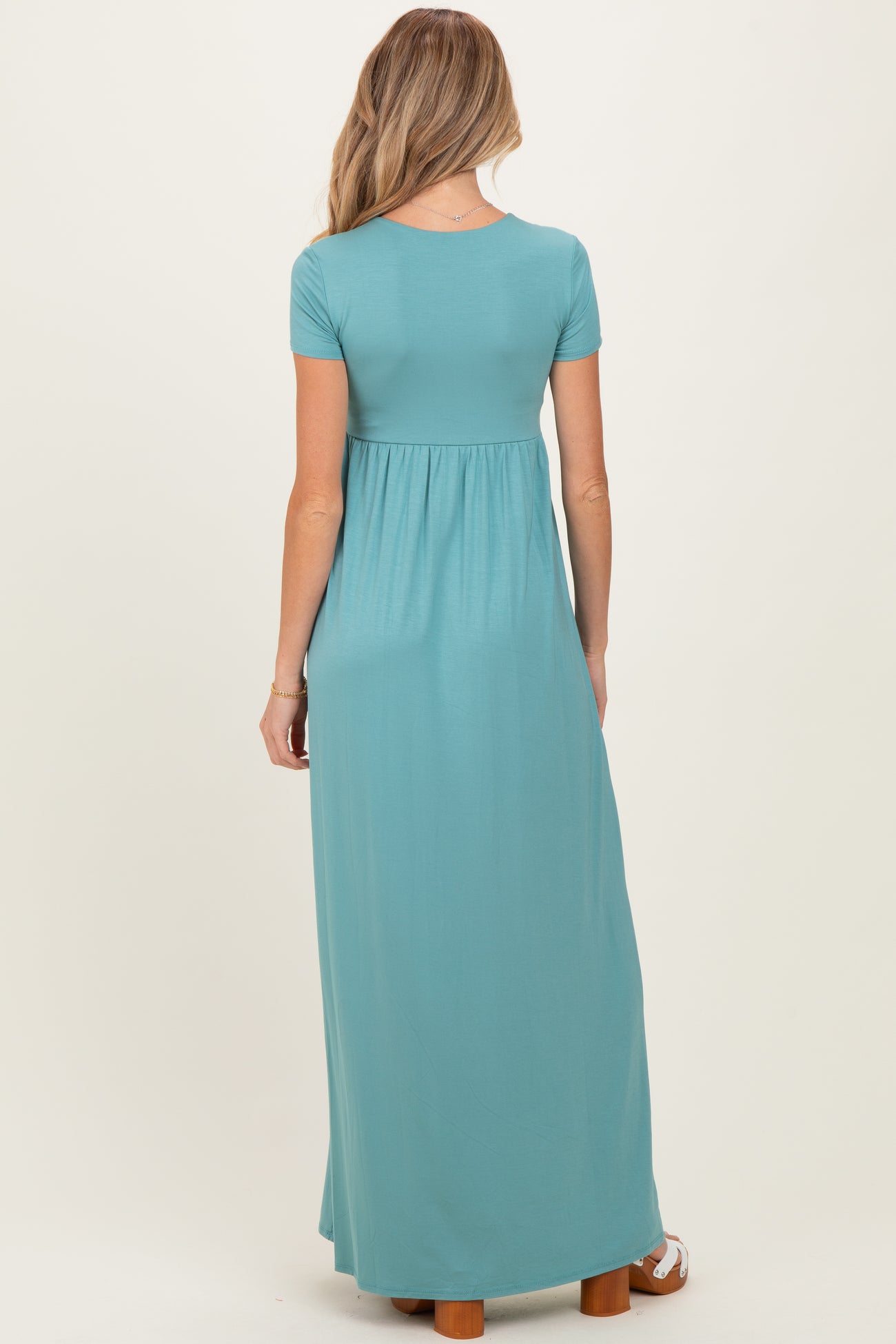 woman wearing a teal short sleeve maxi maternity dress with a fitted bodice and flowing skirt, showing her baby bump