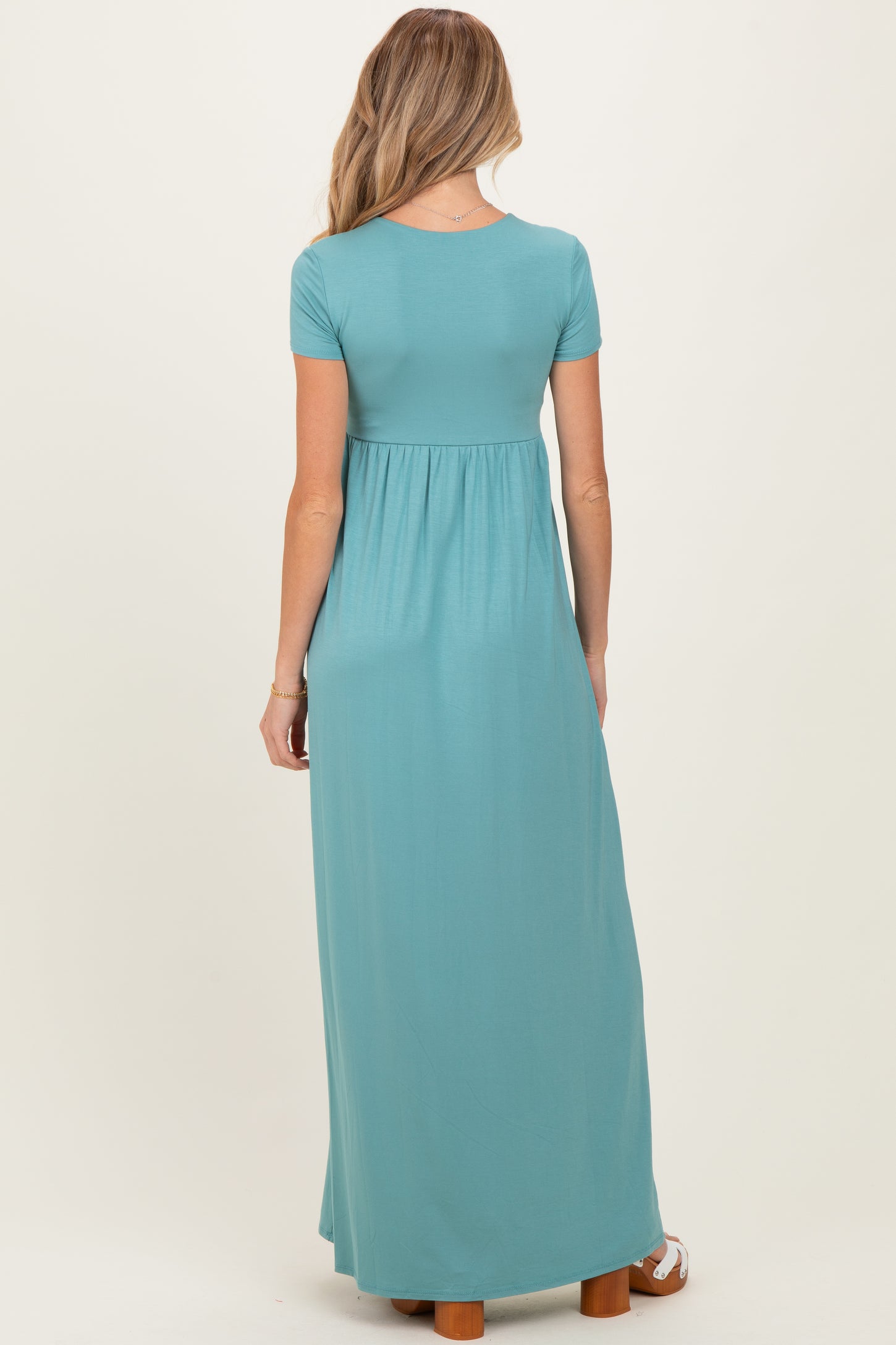 woman wearing a teal short sleeve maxi maternity dress with a fitted bodice and flowing skirt, showing her baby bump