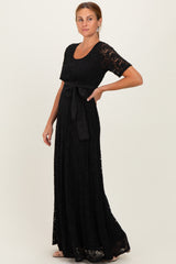 woman wearing a black lace maxi dress with a scoop neckline and a tied waist detail