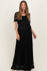 woman wearing a black lace maternity maxi dress with a tie waist and short sleeves, showcasing her baby bump