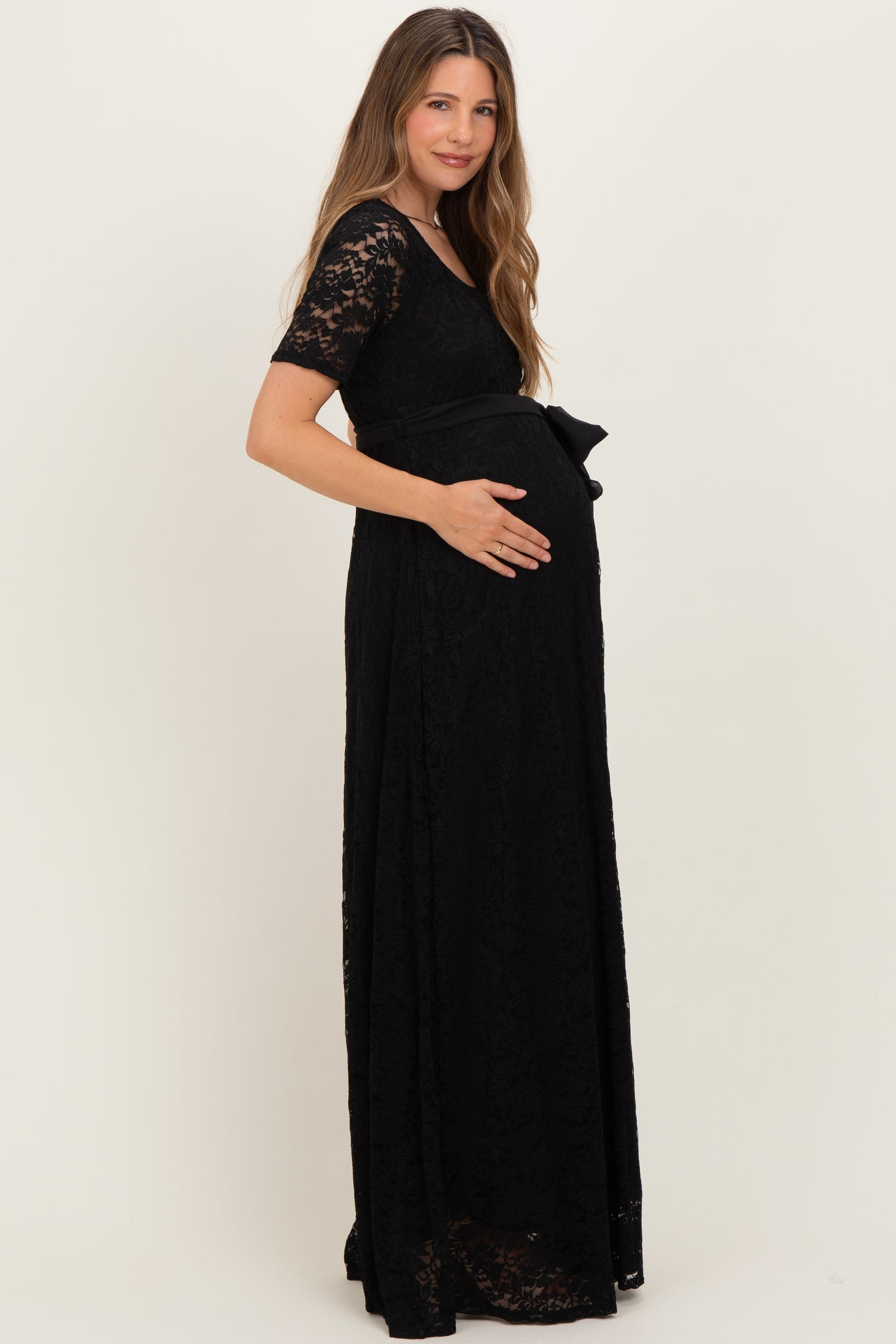 woman wearing a black lace maternity gown with short sleeves and a bow detail, showcasing her baby bump