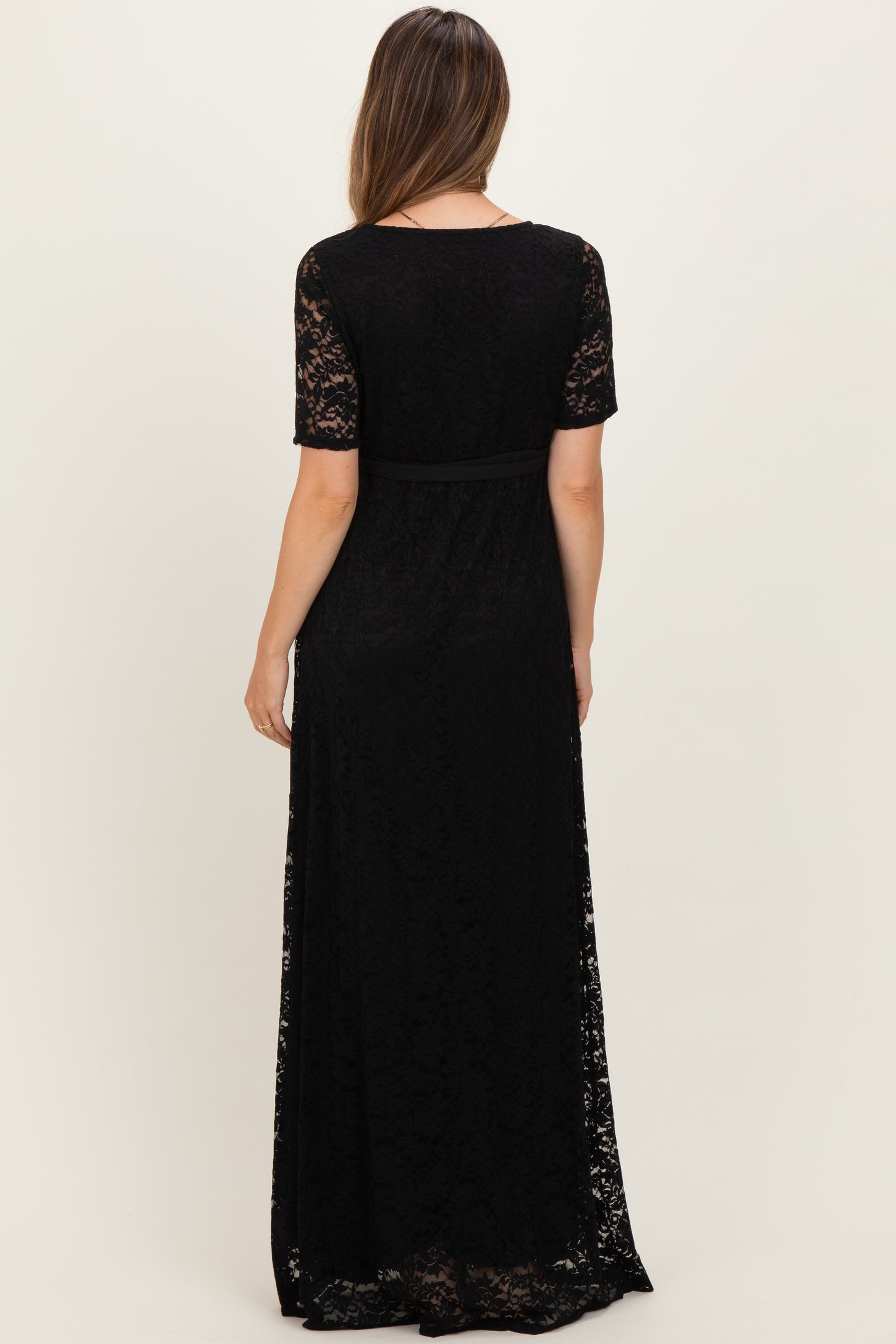 woman wearing a black lace maternity maxi dress with short sleeves and a waist tie, showing the back view