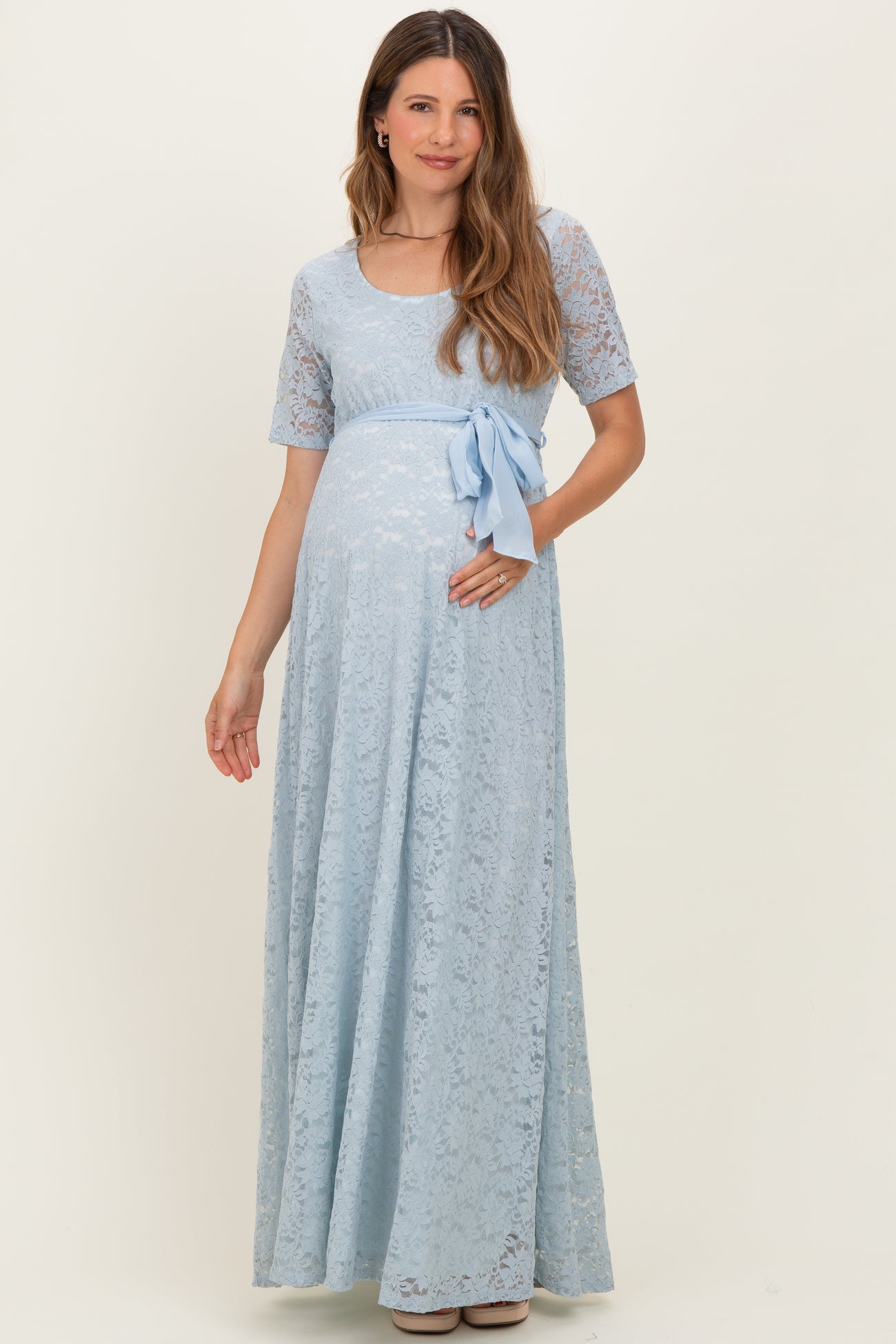 woman wearing a light blue lace maternity maxi dress with a bow accent and a visible baby bump
