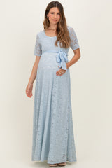 woman wearing a light blue lace maternity maxi dress with a bow accent and a visible baby bump
