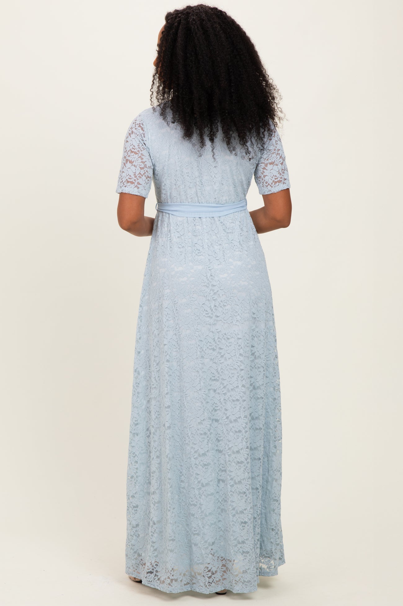 woman wearing a light blue lace maxi dress with short sleeves and a tied waist, shown from the back