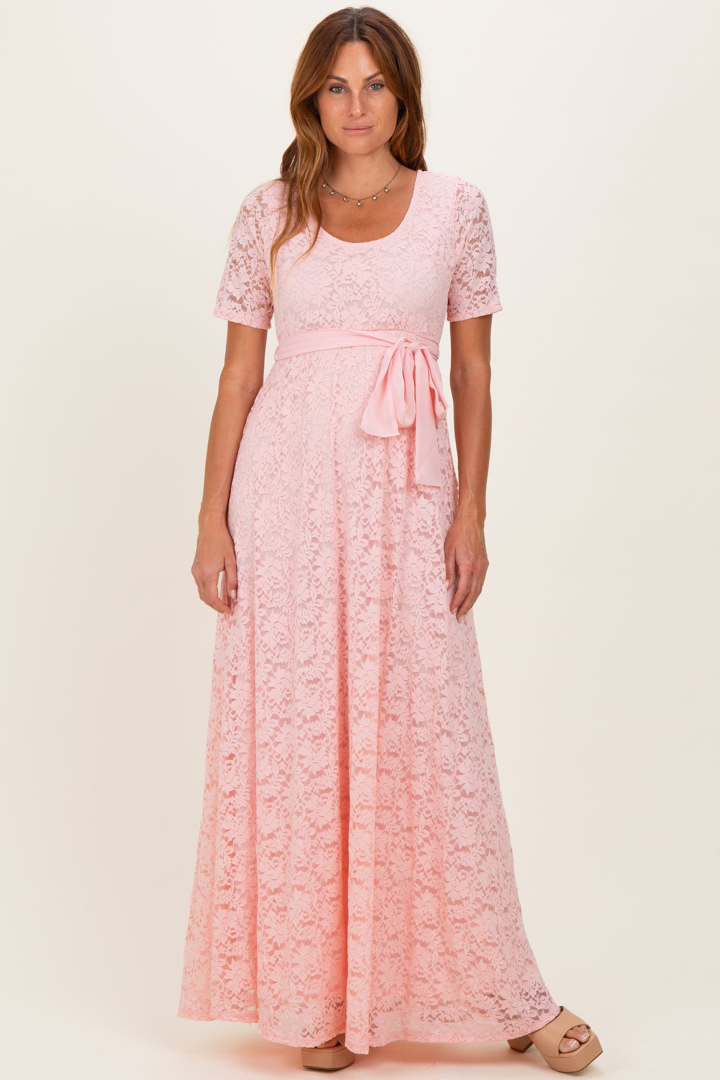 woman wearing a pink lace maxi dress with short sleeves and a waist tie detail