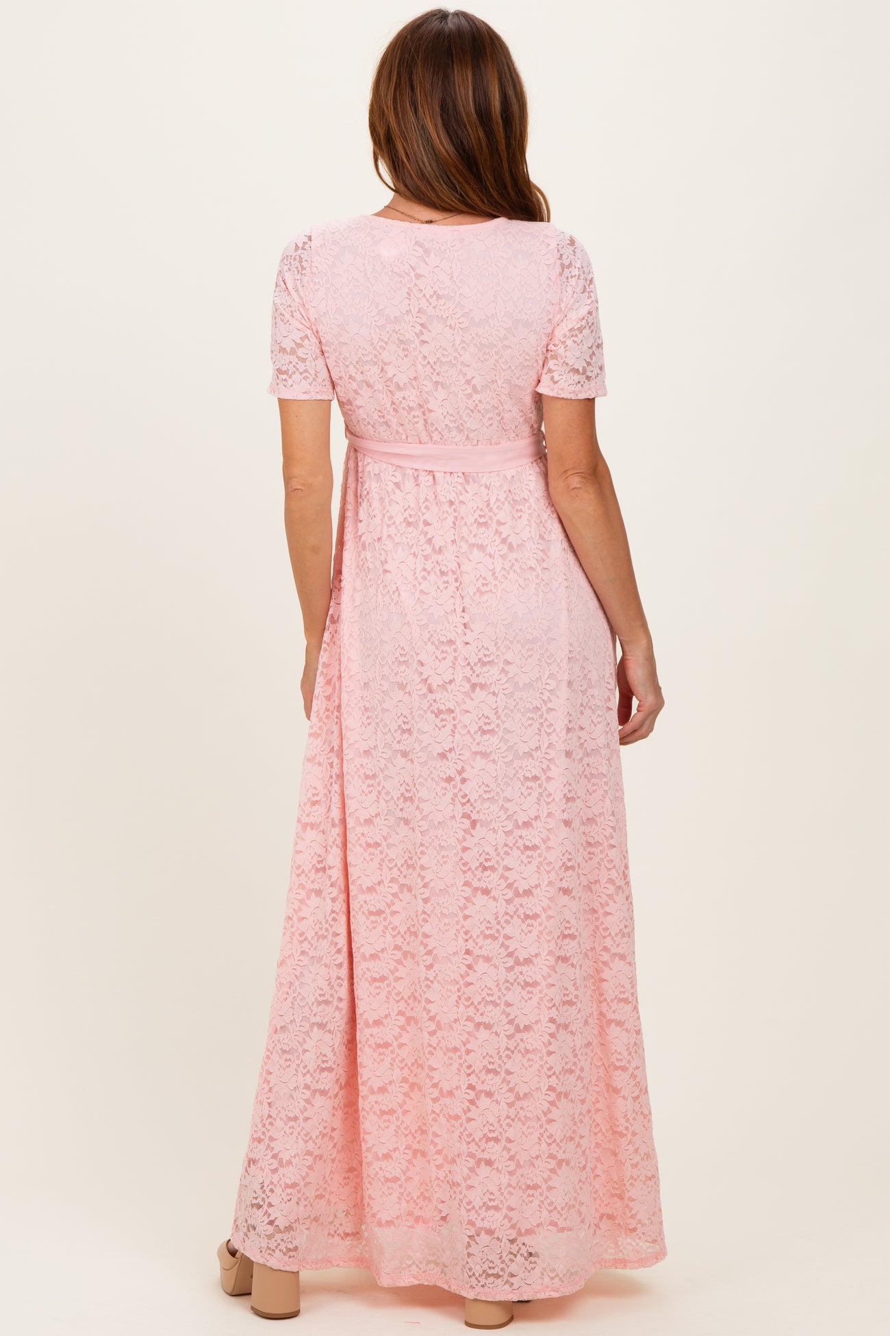 woman wearing a pink lace maxi dress with short sleeves and a tied waist detail, shown from the back