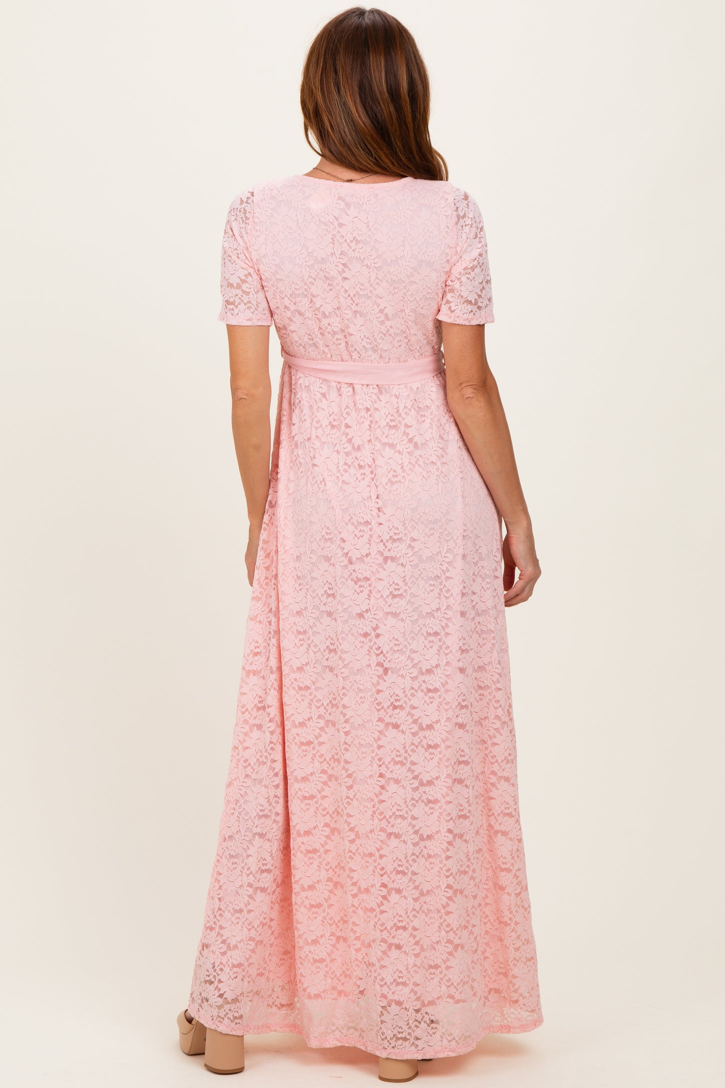 woman wearing a pink lace maxi dress with short sleeves and a tied waist detail, shown from the back