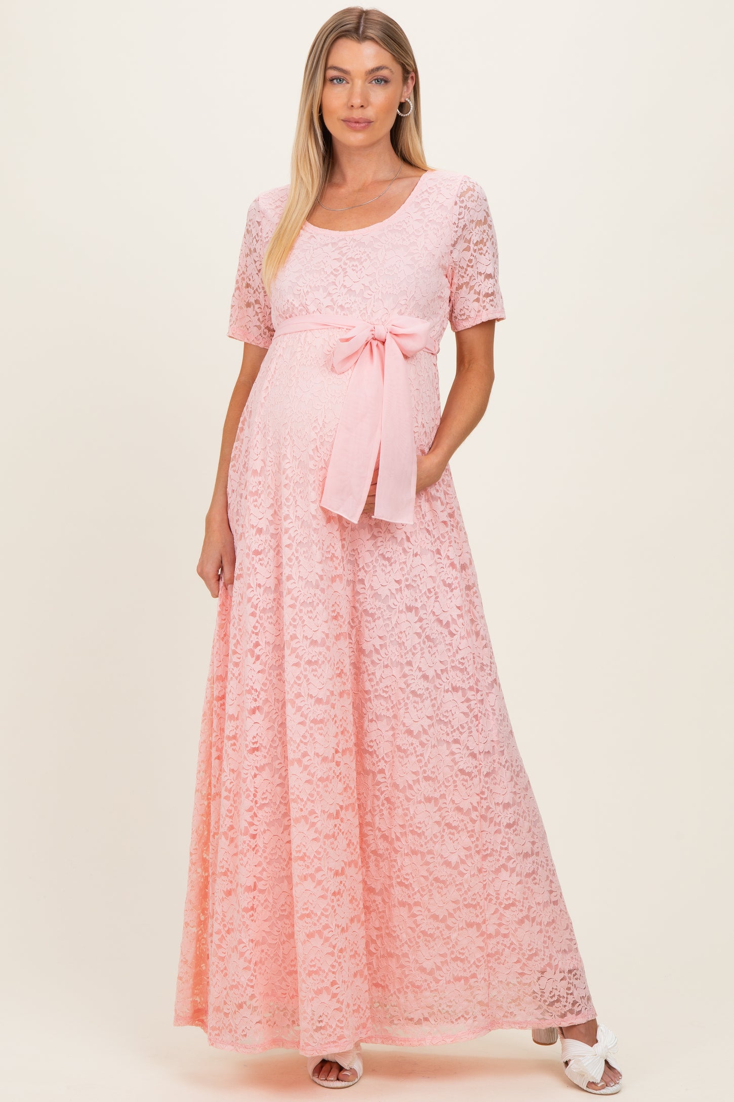 woman wearing a pink lace maternity dress with short sleeves and a bow detail, showing her baby bump