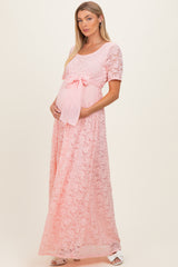 woman wearing a pink lace maternity gown with short sleeves and a bow tie at the waist, highlighting her baby bump