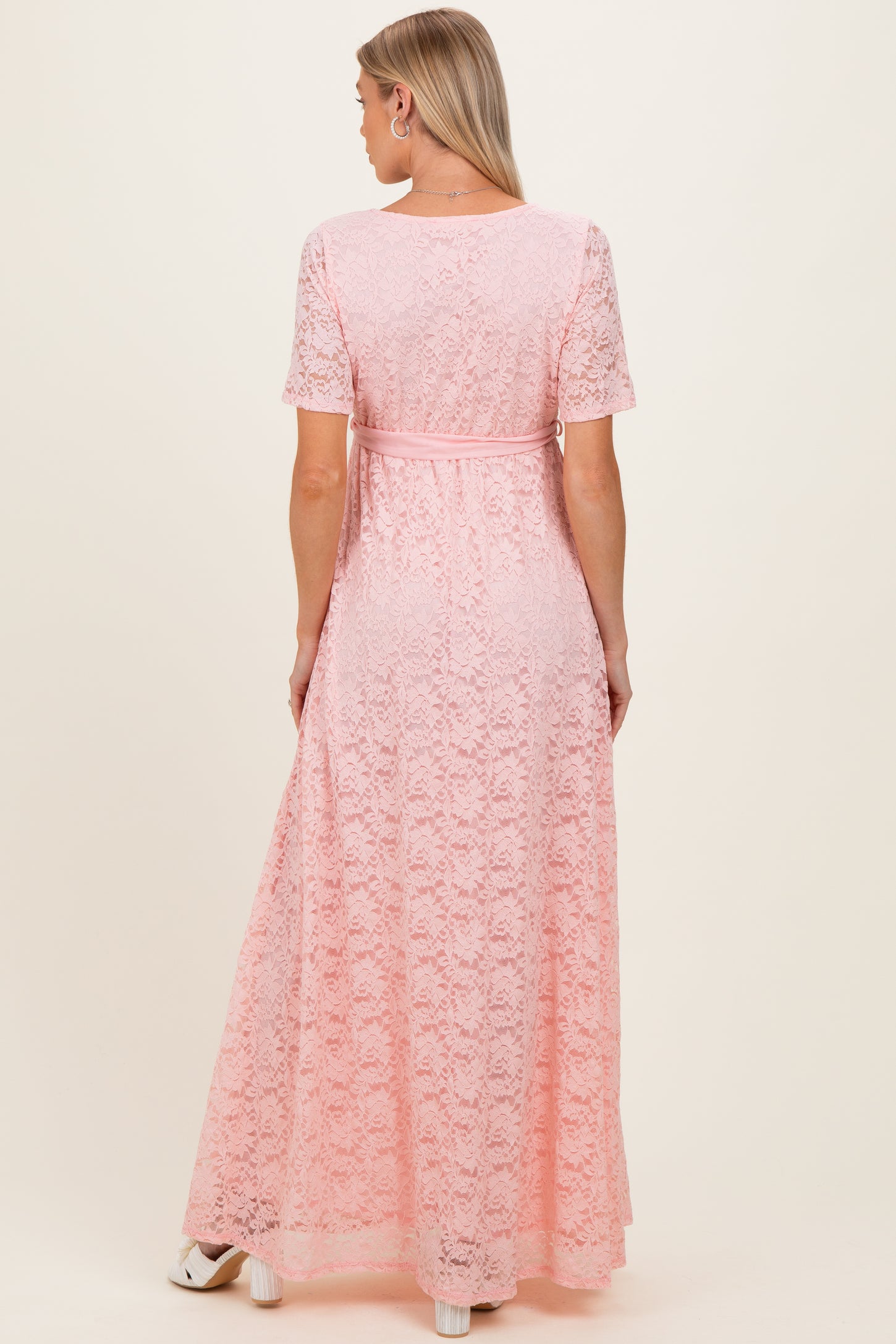 woman wearing a blush pink lace maternity maxi dress with a belted waist and short sleeves