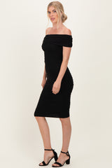 woman wearing a black off-the-shoulder bodycon dress with ruching details and strappy black heels
