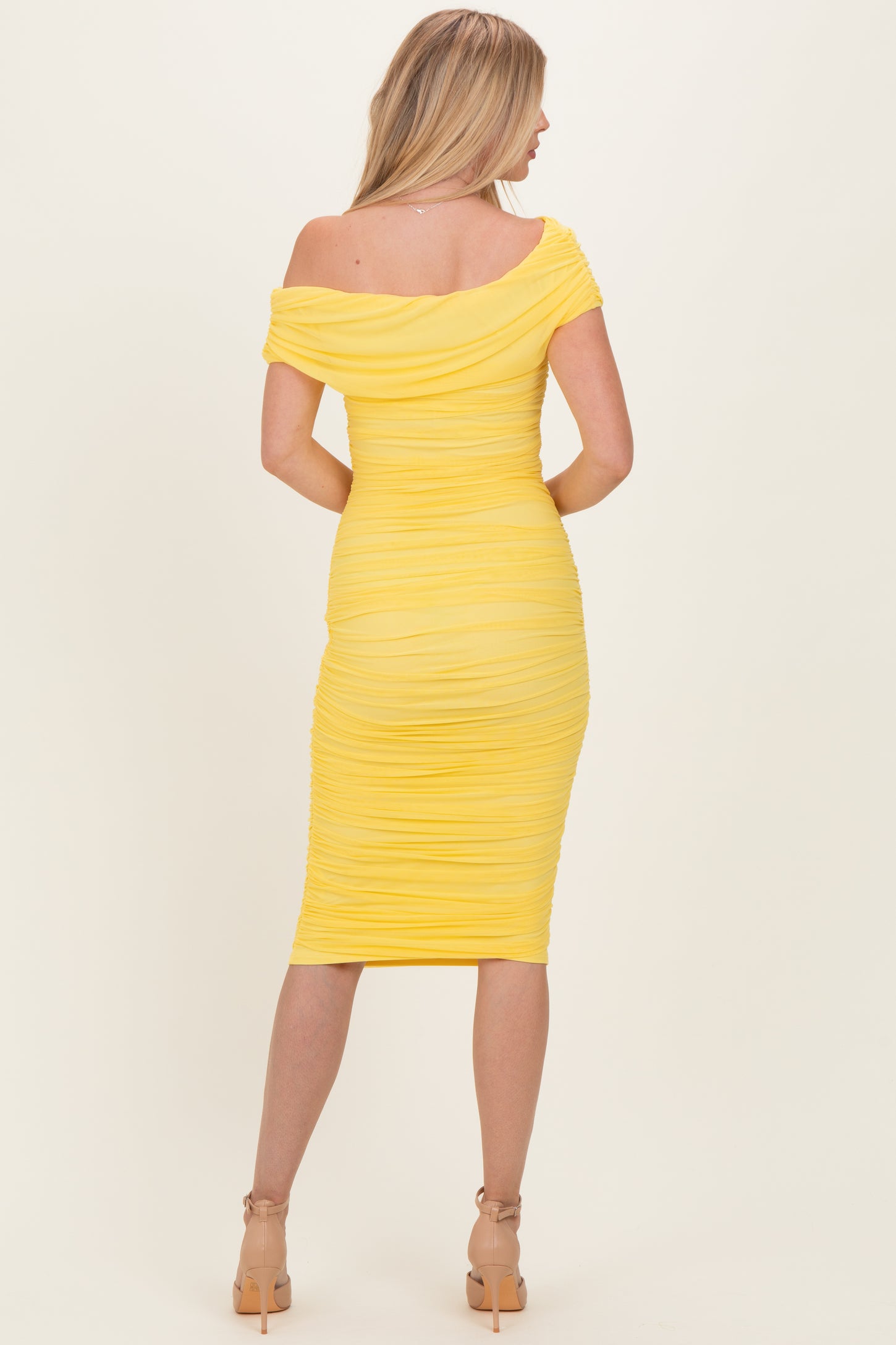 woman wearing a yellow off-shoulder bodycon dress with ruched detailing, viewed from the back