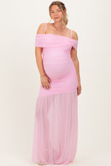 woman wearing a light pink off-the-shoulder maternity gown with ruched detailing and sheer skirt, showcasing her baby bump