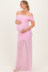 woman wearing a pink off-the-shoulder maternity gown with ruched details and holding her baby bump