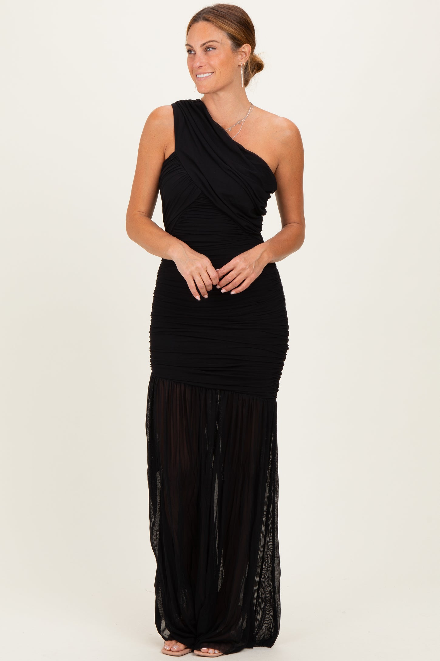 woman wearing a black one-shoulder ruched maxi dress with a sheer skirt detail
