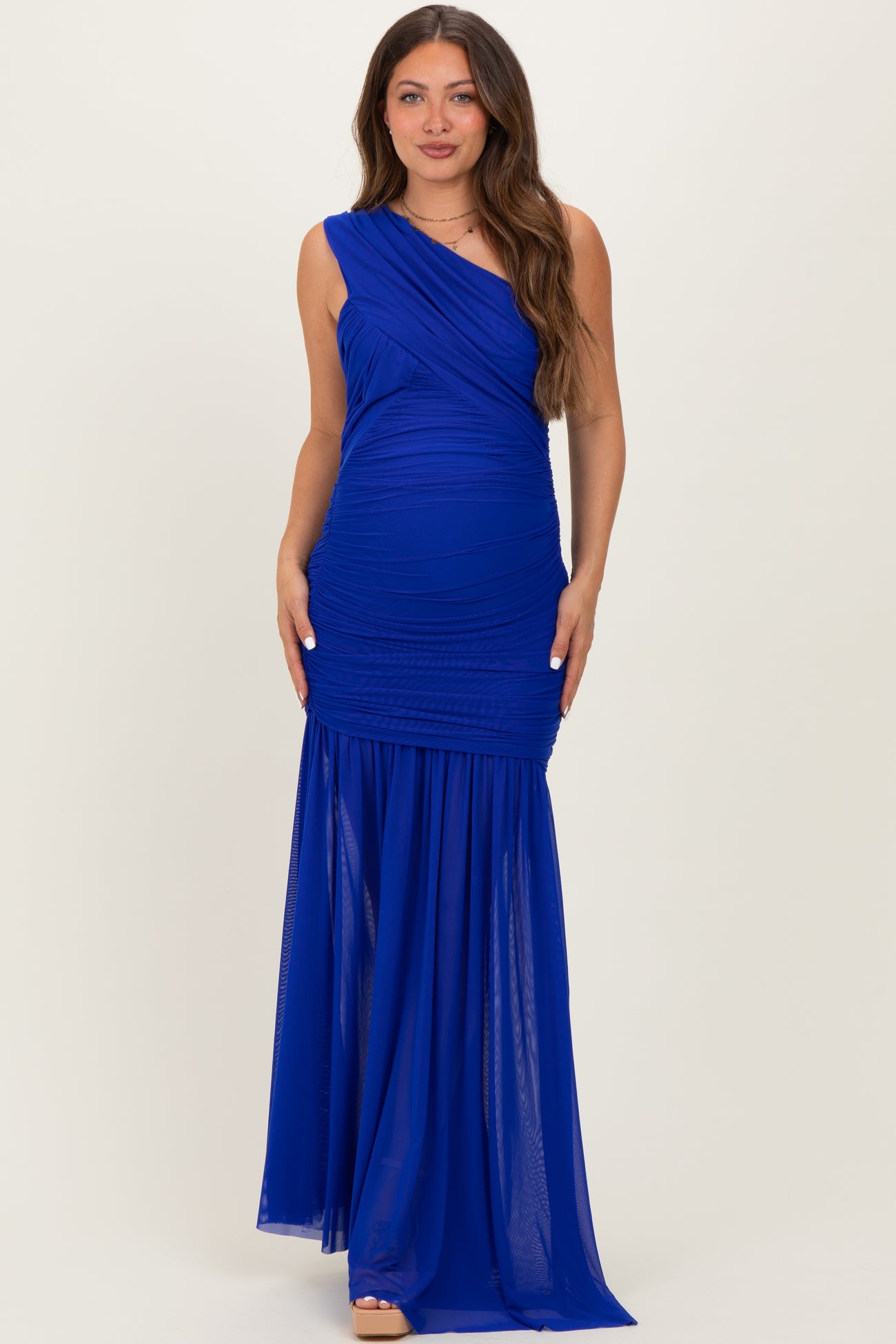 woman wearing a royal blue one-shoulder maternity gown with ruched detailing and a flowing skirt
