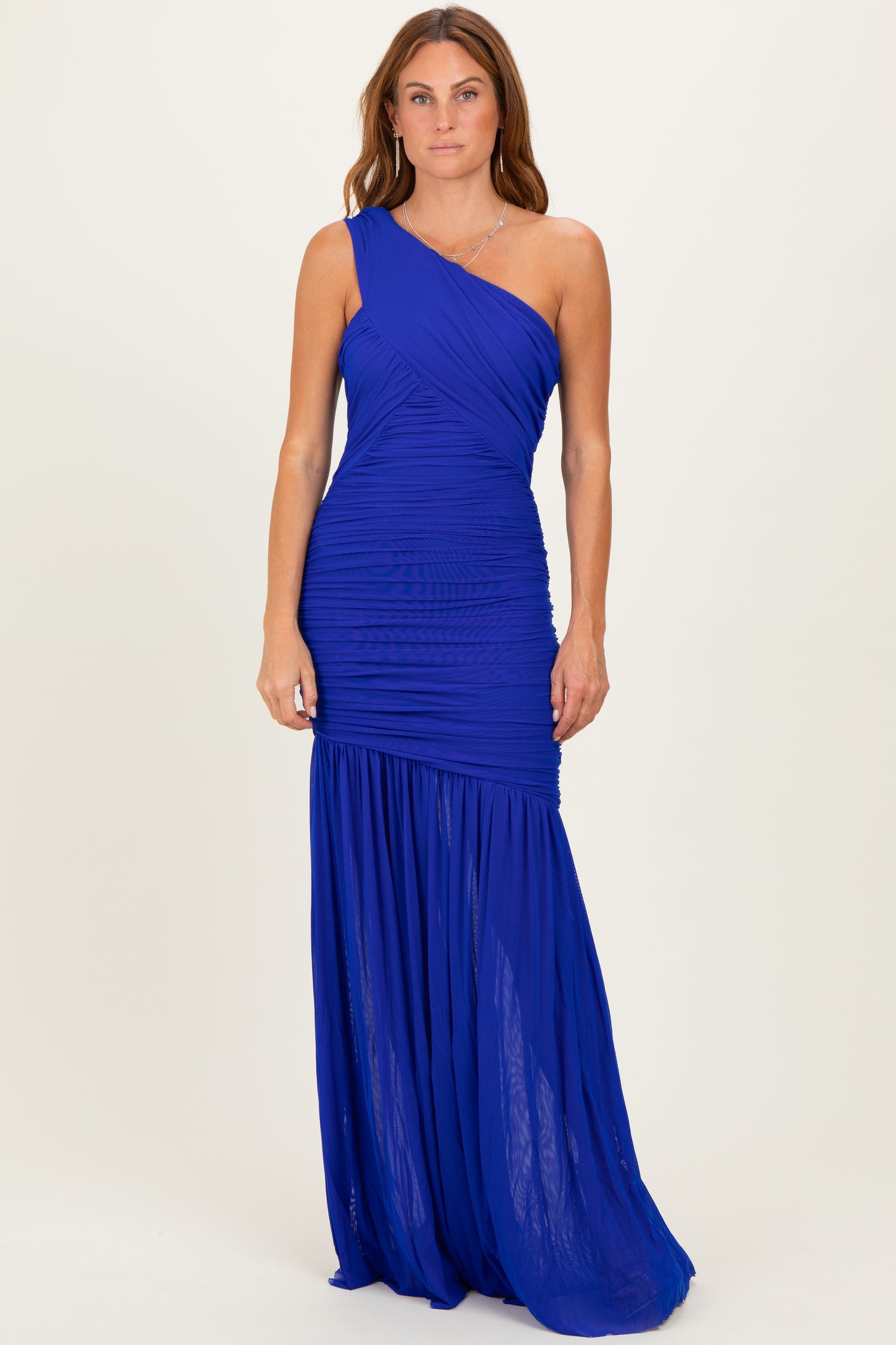 woman wearing a royal blue one-shoulder maxi dress with ruched details and a flowing skirt