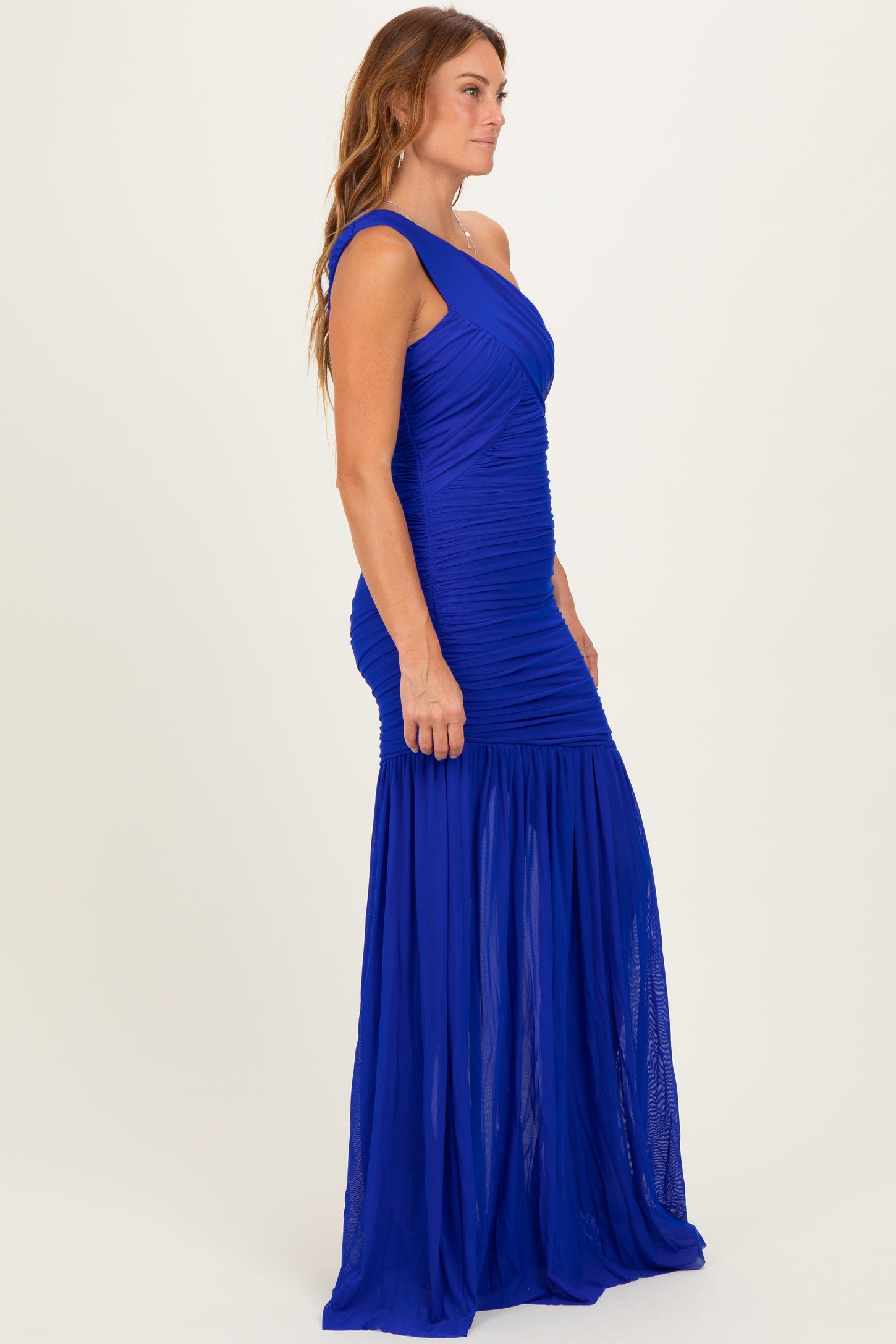 woman wearing a royal blue one-shoulder evening gown with ruched detailing and a flared skirt