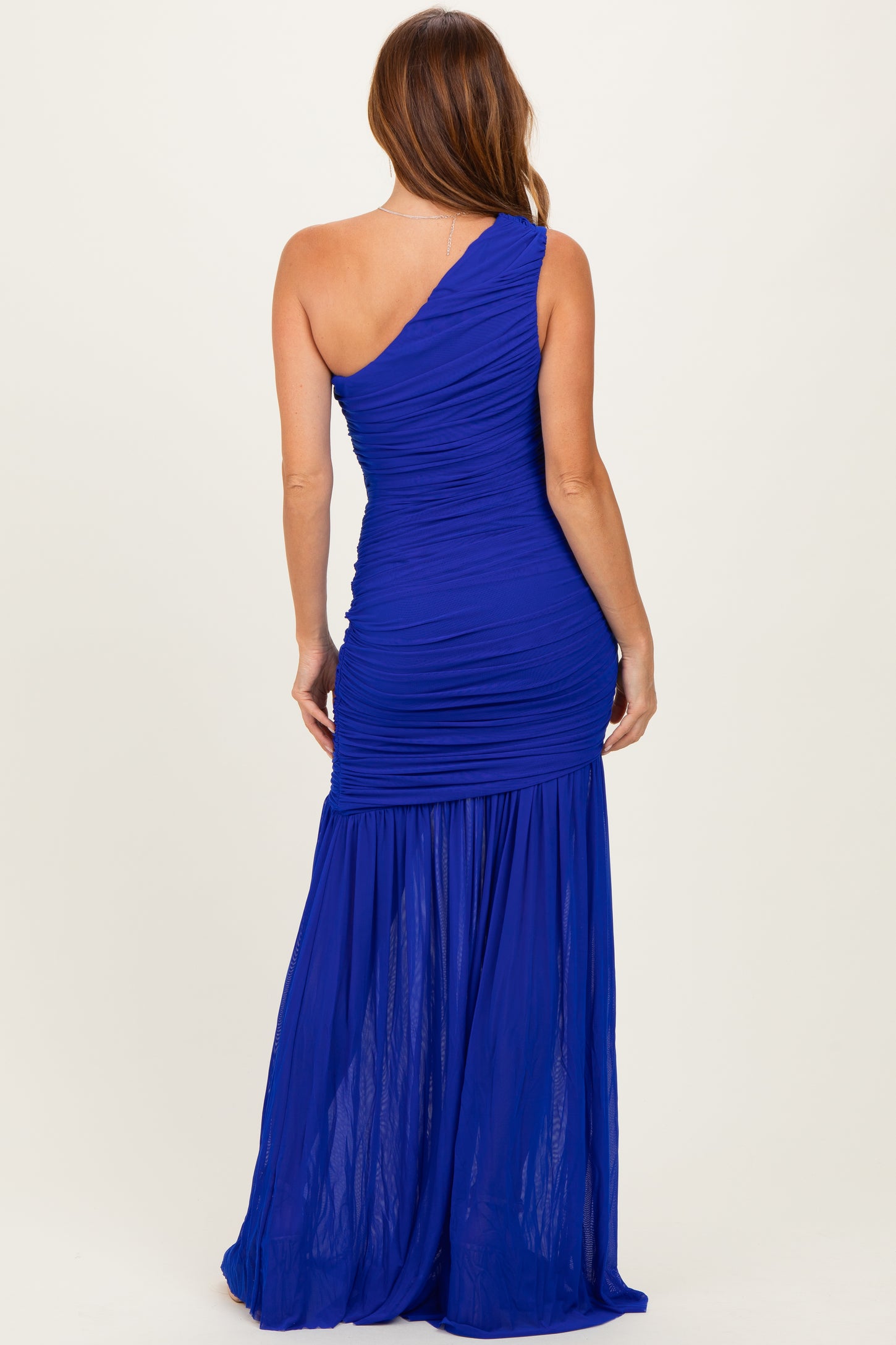 woman wearing a blue one-shoulder ruched evening gown with a flowing skirt and fitted bodice from the back