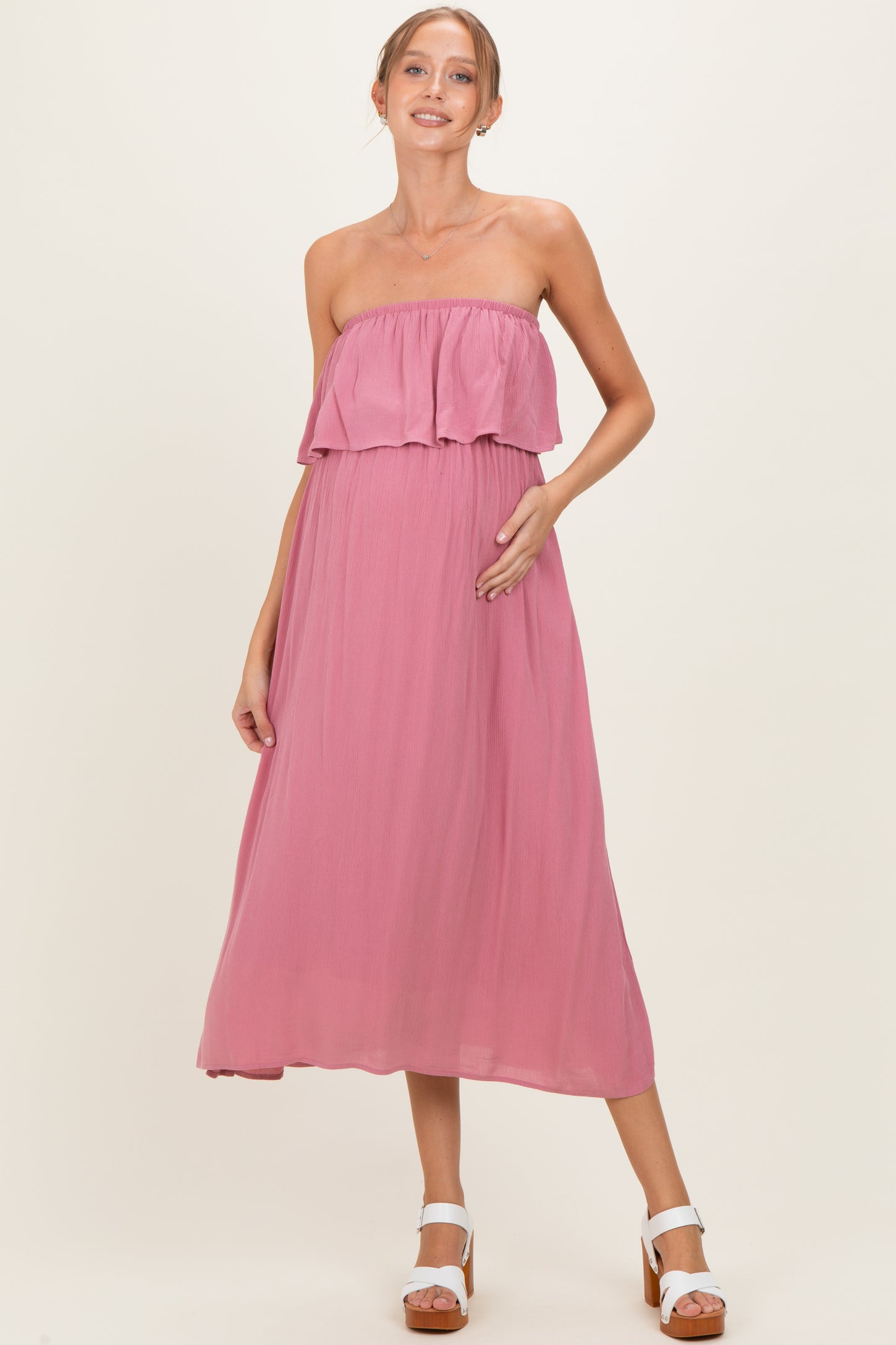 woman wearing a strapless pink maternity maxi dress with a ruffled top and holding her baby bump