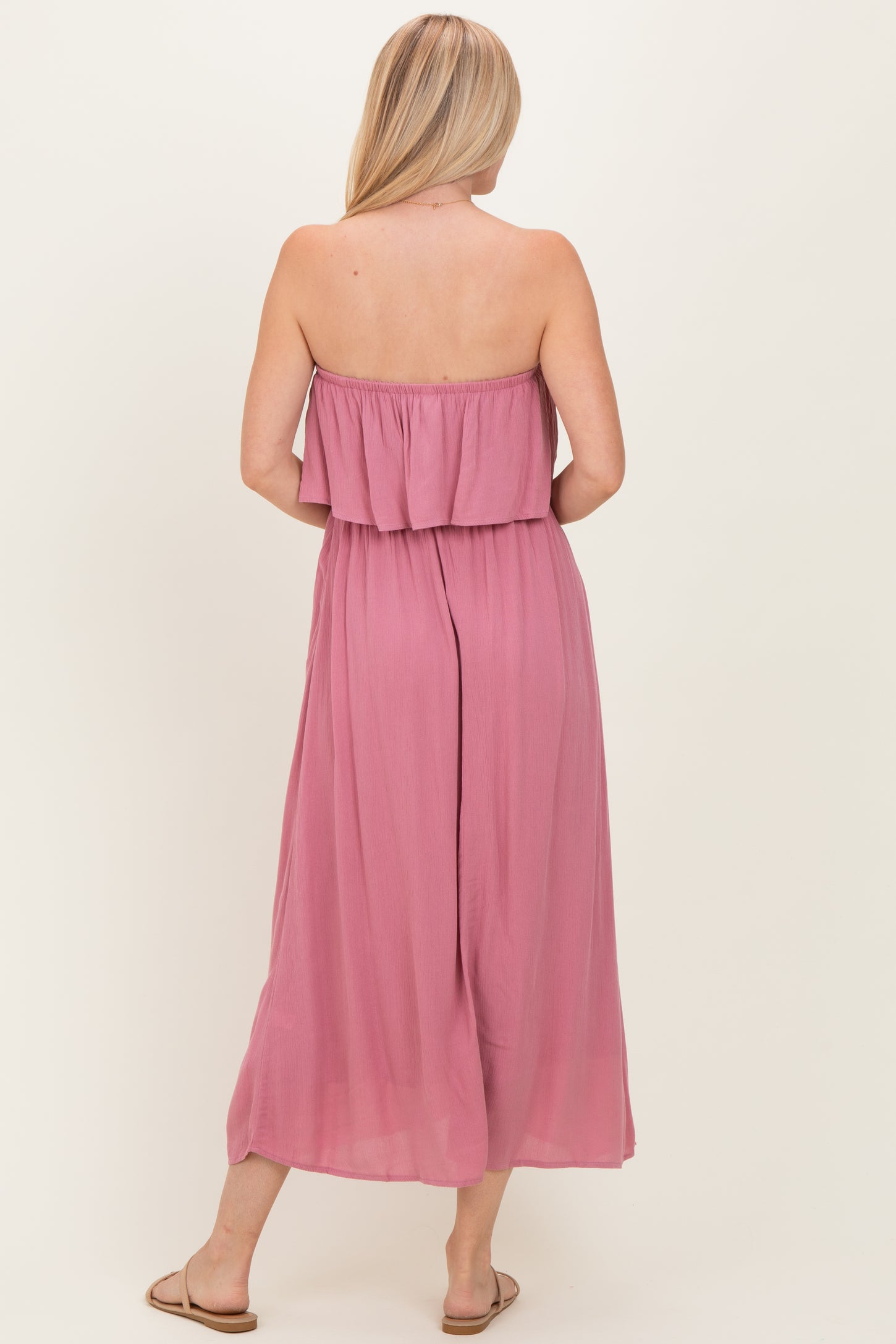 back view of a woman wearing a strapless mauve maxi dress with a flowy design and a ruffled bodice