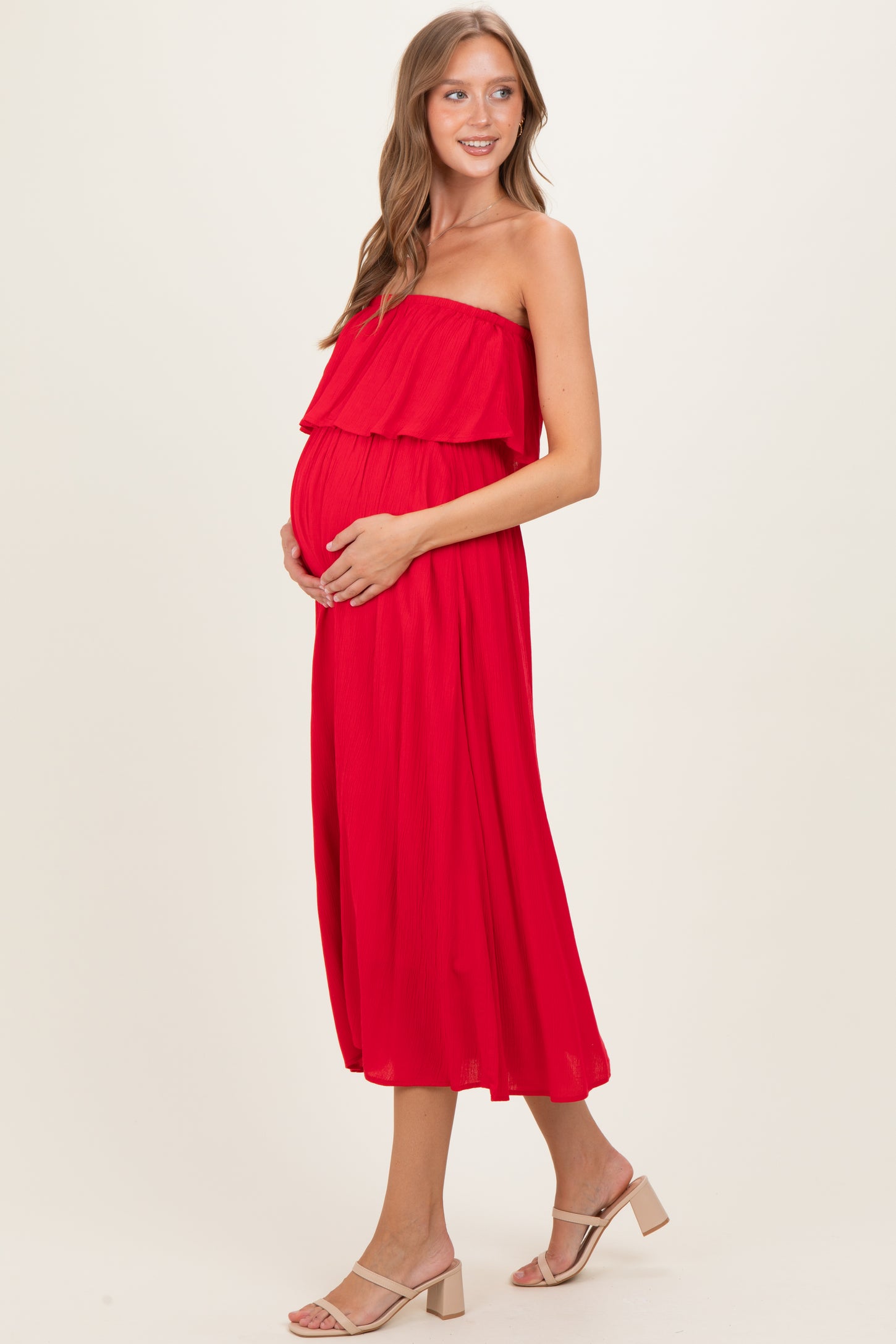 woman wearing a vibrant red maternity dress with a layered ruffle design and holding her baby bump