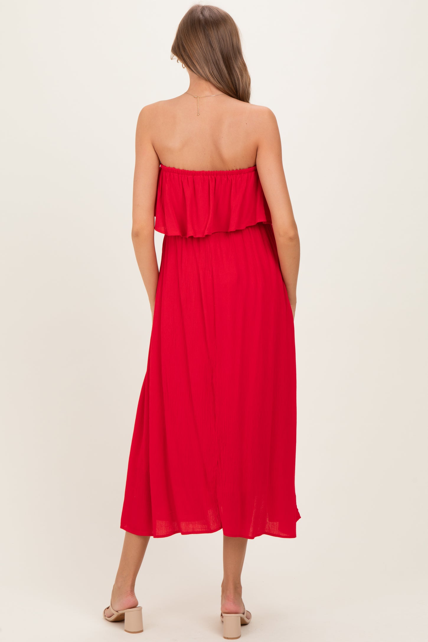 woman wearing a red strapless maternity maxi dress with ruffle detail, showcasing a flowing silhouette from the back