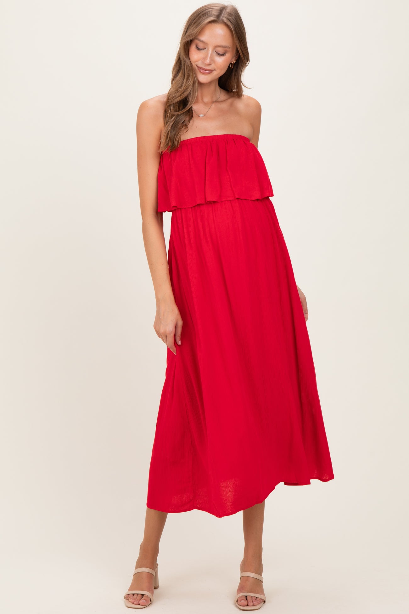 woman wearing a red strapless maternity maxi dress with ruffle detail and flowing silhouette