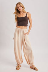 woman wearing a brown fitted tank top and light peach harem pants with pockets, paired with casual sandals