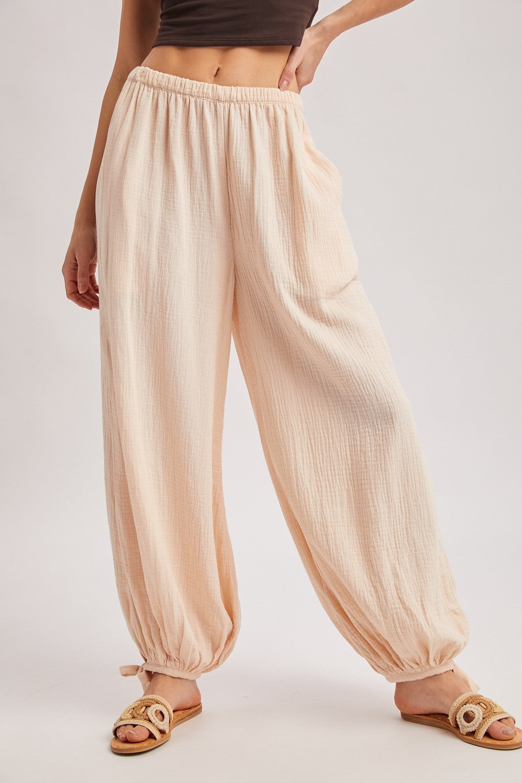 woman wearing light peach wide-leg pants with an elastic waistband and tapered ankles, styled with open-toe sandals