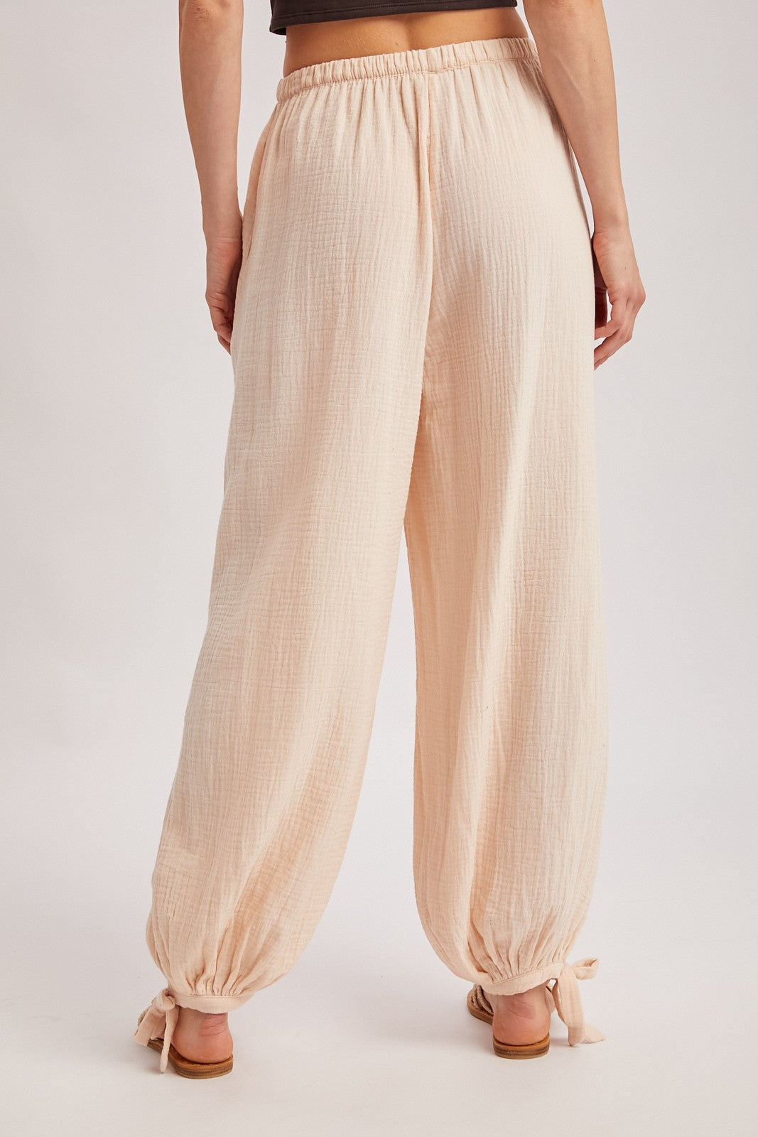 woman wearing light pink loose-fitting pants with elastic waistband and adjustable tie at the ankles, seen from behind