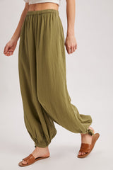 woman wearing olive green loose-fitting trousers with elastic cuffs and a high waistband, paired with brown slide sandals