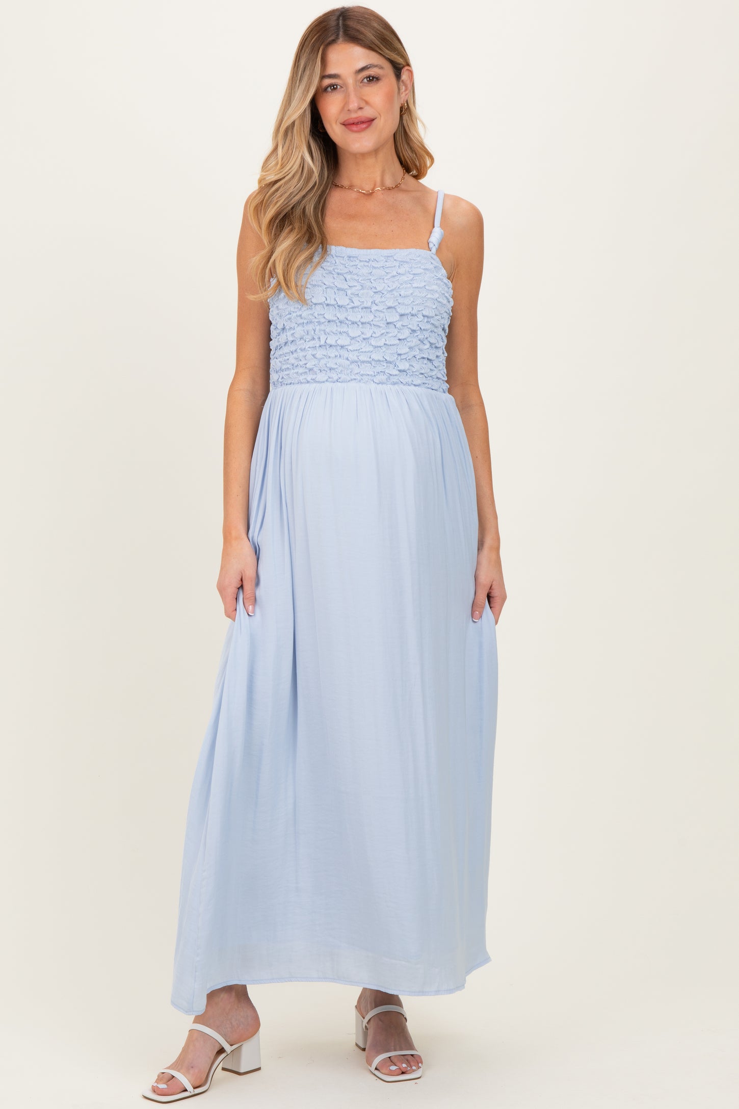 woman wearing a light blue maternity maxi dress with smocked bodice and adjustable straps, showcasing her baby bump