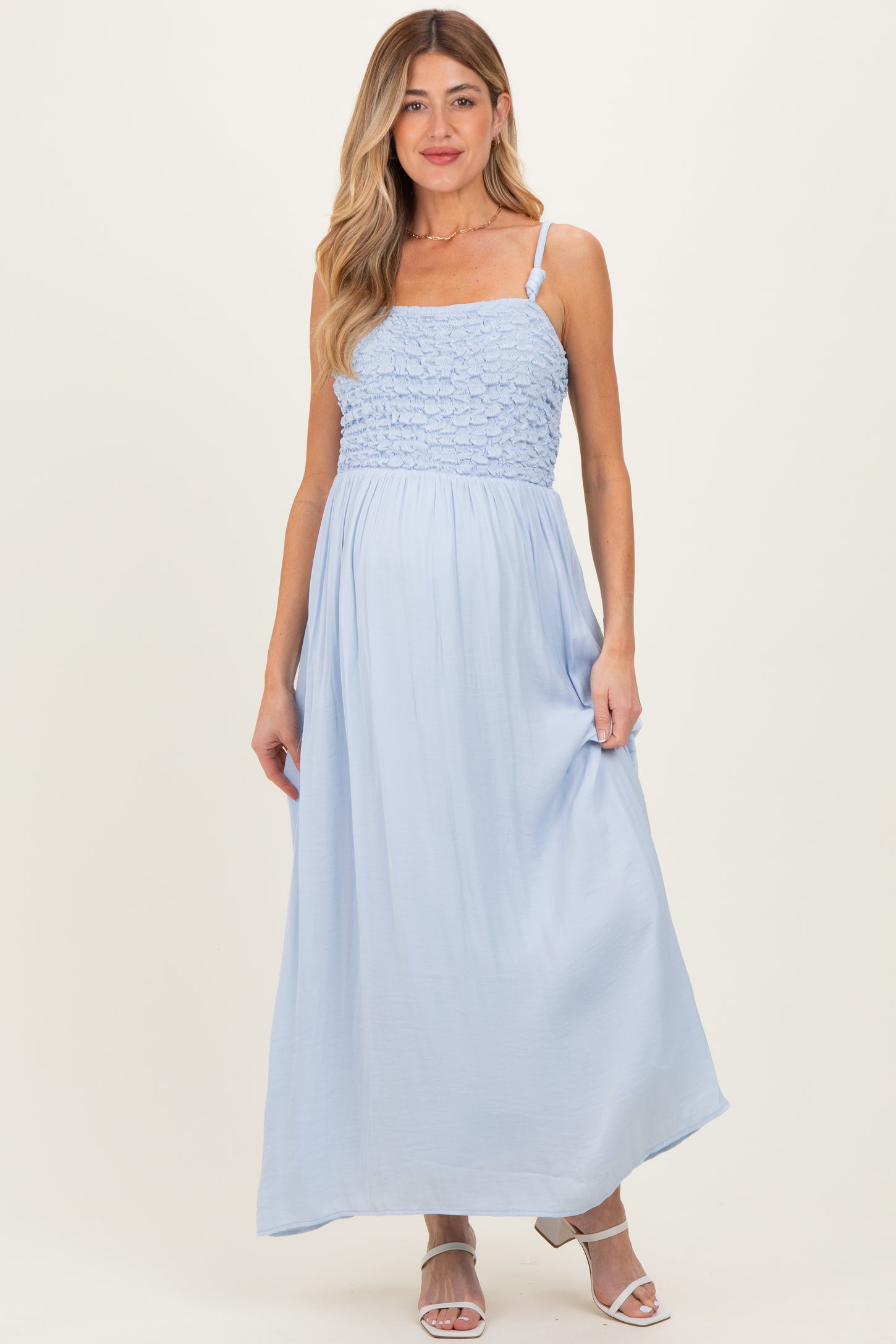 woman wearing a light blue maternity maxi dress with a smocked bodice and adjustable straps, and showing a baby bump