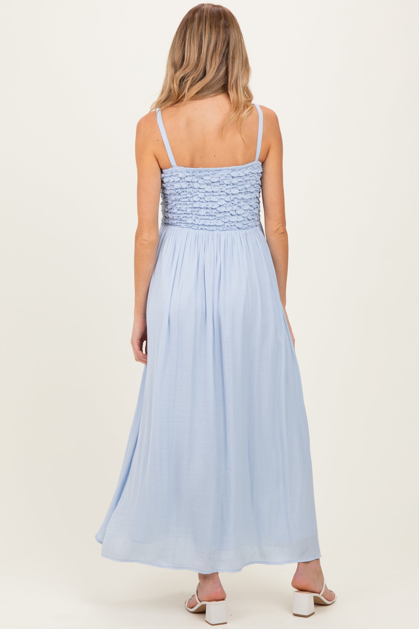 woman wearing a light blue maternity maxi dress with a smocked bodice and thin straps, showing her baby bump from the back
